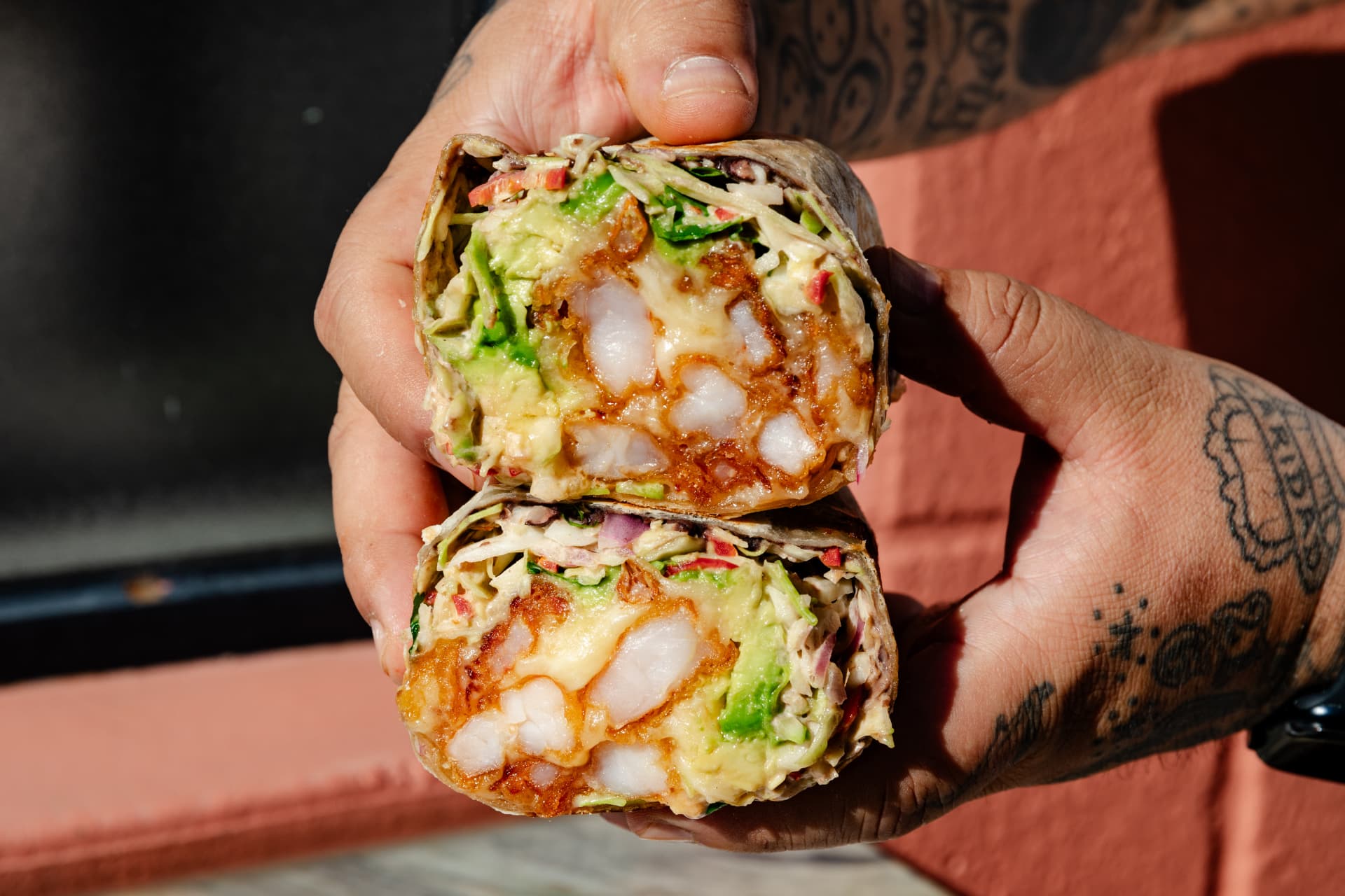 Shrimp burrito halved and held over a terracotta wall