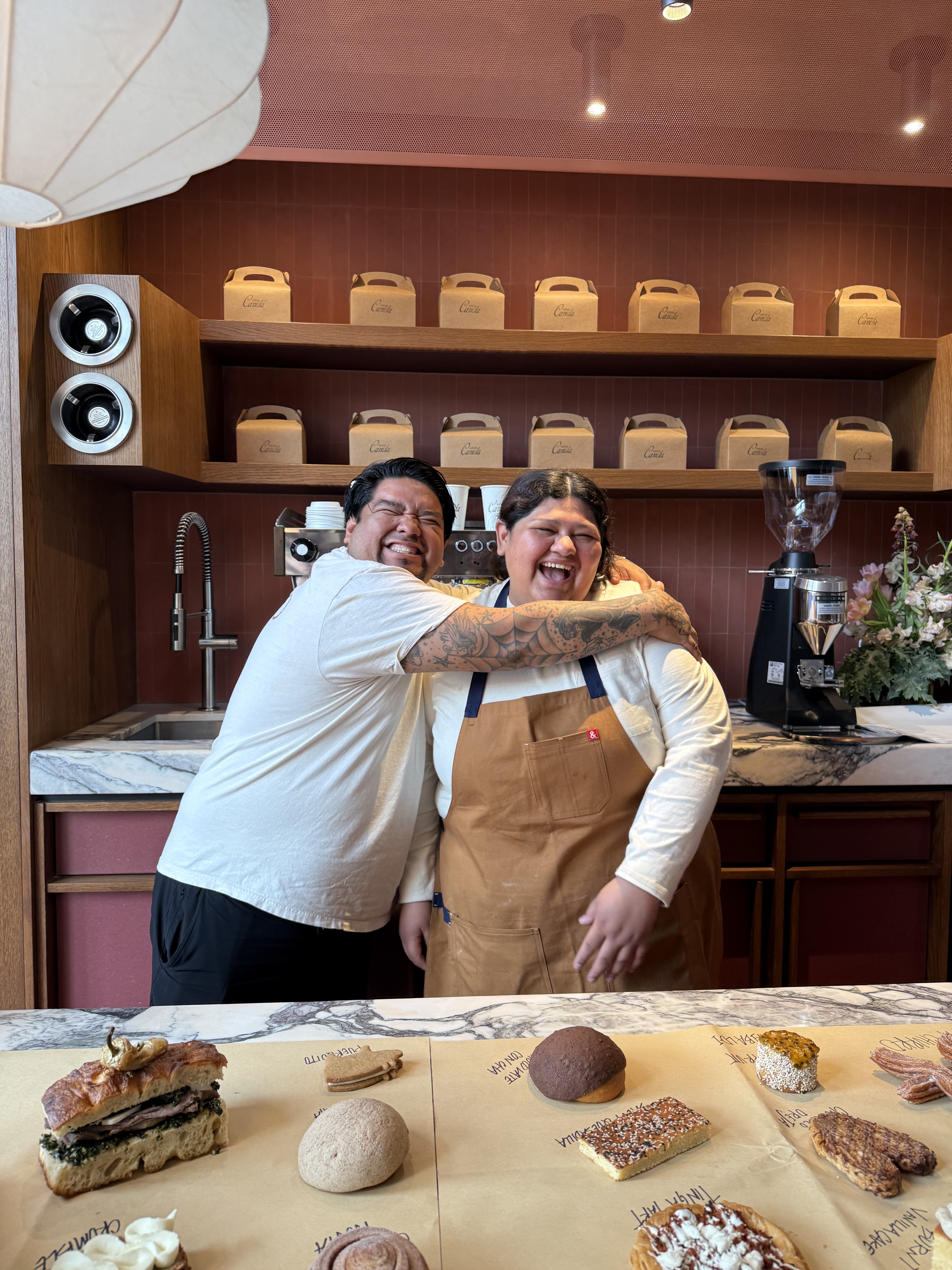 Two bakers laughing behind the Santa Canela counter